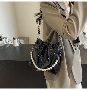Detail of black patent leather bucket bag with white pearl handle and glossy texture