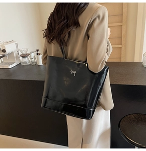 Close-up of black glossy patent leather tote bag with a silver metal bow detail