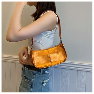 Sac à bandoulière orange métallisé avec rivets argentés porté par un mannequin en extérieur