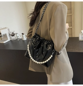 Quilted black patent leather handbag with pearl handle shown on shoulder of a female model