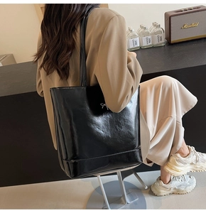 Close-up of black glossy PU tote bag with silver bow hardware on beige suit
