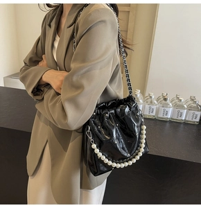 Detail of black glossy PU bucket bag with white pearl handle and metal chain strap
