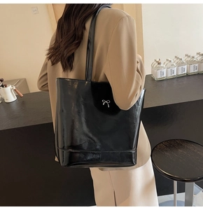 Detail of black glossy PU leather tote bag with silver bow ornament and long shoulder straps