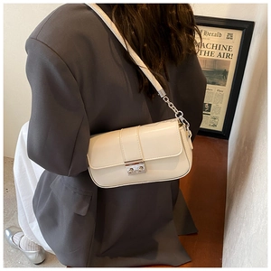 Detail of cream PU leather shoulder bag with silver metal buckle and chain strap on model