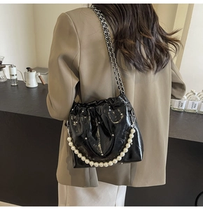 Detail of black patent leather bucket bag with elegant pearl strap and metal chain