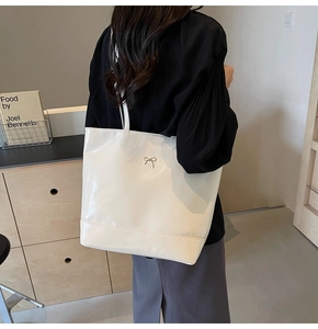 Detail shot of a cream glossy PU tote bag with a delicate metal bow accent and smooth finish