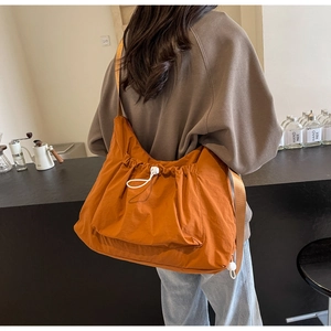 Model wearing a large caramel orange crossbody bag with adjustable wide strap and drawstring