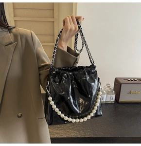 Detail of glossy black PU bucket bag with silver studs, chain strap, and pearl handle