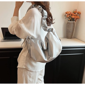 Silver PU leather crescent bag with wide pleated shoulder strap worn by a female model