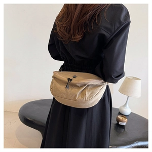 Detail shot of khaki nylon waist bag with black zipper on model wearing black dress