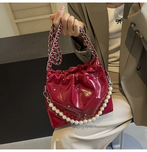 Detail of red quilted PU leather bucket bag with glossy finish and pearl chain accessory