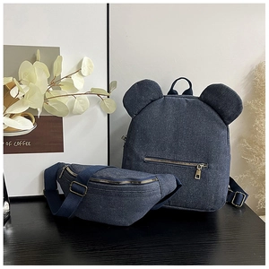 Navy denim backpack with bear ear design and matching waist bag set on dark wood