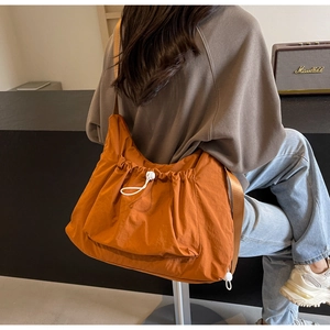 Detailed side view of orange nylon crossbody bag with drawstring closure on model