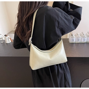 Detail shot of a beige crescent PU leather shoulder bag worn by a model in a modern cafe