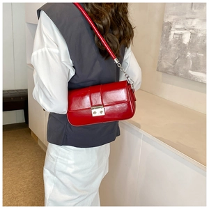 Close-up of bright red patent leather crossbody bag with silver buckle and metal chain strap