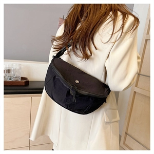 Detail of black nylon crescent crossbody bag with adjustable strap on a white blazer