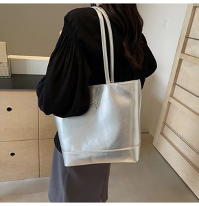 Detail of silver metallic PU tote bag with a small bow charm worn by a model