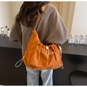 Detail of orange drawstring crossbody bag with pleated texture and wide shoulder strap