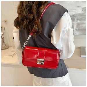 Detail of red glossy patent leather shoulder bag with metal buckle and silver chain strap