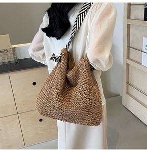 Détail d'un sac en paille tressée avec une large bandoulière rayée noire et blanche