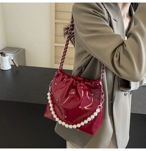 Detail of red quilted bucket bag featuring silver rivets and elegant pearl chain handle
