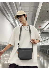 Detail view of a minimalist dark gray crossbody bag with a vibrant orange accent tag