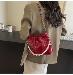 Close-up of red patent leather bucket bag with pearl handle and metal chain strap