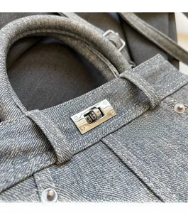 Gros plan d'un sac bandoulière en denim bleu avec un fermoir tournant en métal argenté