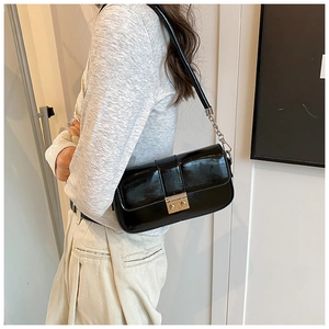 Close-up of black glossy PU leather baguette bag with gold buckle and chain strap detail
