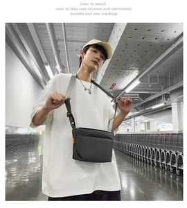 Detail of minimalist black crossbody bag with decorative orange tag on a male model