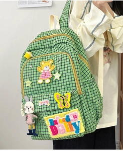 Detail of green plaid nylon backpack featuring cute embroidery patches and a rabbit charm
