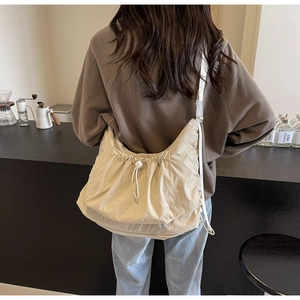 Detail of a casual beige drawstring crossbody bag with adjustable white strap in a cafe setting