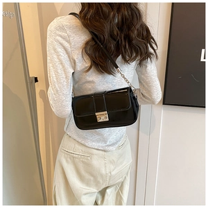 Rear view of a model wearing a black glossy patent leather shoulder bag with a gold clasp