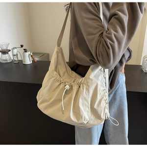 Detailed shot of large cream fabric crossbody bag featuring stylish drawstring accents