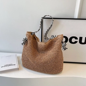 Sac à bandoulière en paille tissé avec des nœuds en ruban rayé noir et blanc sur fond blanc