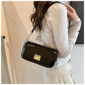 Detail of black patent leather baguette bag with silver buckle and chain shoulder strap