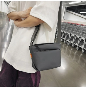 Detail of grey crossbody bag featuring a matte finish and a bright orange side tag