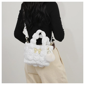 Détail d'un sac bandoulière blanc matelassé avec nœud doré et pendentif boule en peluche