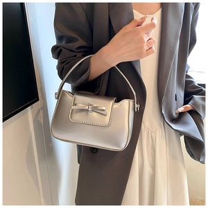 Detail view of a silver metallic mini handbag with bow decoration and glossy finish