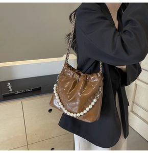 Detailed view of brown glossy bucket bag with pearl chain and elegant diamond stitching