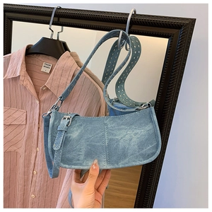Détail du sac bandoulière en denim bleu avec rivets métalliques et large sangle réglable