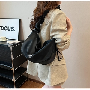 Detail of black pleated PU leather crossbody bag with metal plaque on wide shoulder strap