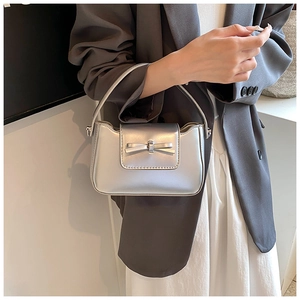 Detail view of a silver PU crossbody bag with a bow accent worn by a model