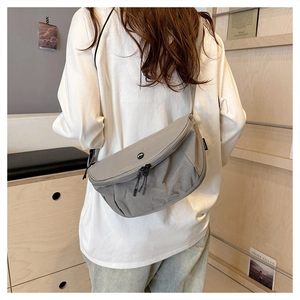 Detail of grey washed fabric crossbody bag featuring a round logo and adjustable strap
