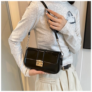 Close-up of black patent leather underarm bag with silver square buckle and chain strap