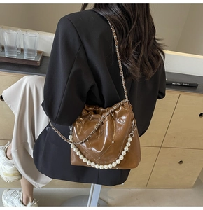 Detail of a brown quilted PU bucket bag with elegant pearl strap and chain on a model