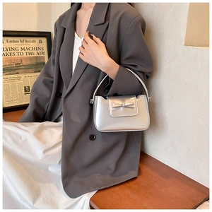 Close-up of a metallic silver PU leather handbag with a bow detail in a stylish setting