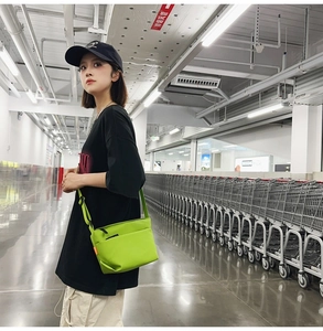 Detail showing neon green crossbody bag with front zipper pocket and adjustable strap