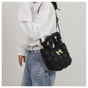 Détail du sac à main en nylon matelassé noir avec nœud doré et bandoulière amovible