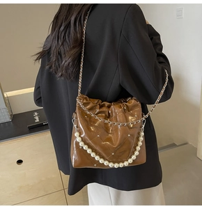 Close-up of brown quilted PU leather bucket bag with large pearl chain and silver strap